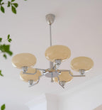 Clérachic five-head chrome chandelier with cream globes and a small hub finial, plant leaves at the left.