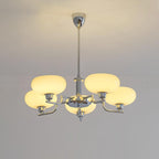 Clérachic five-head chrome chandelier lit, five flattened globes glowing above a moulded off-white wall.