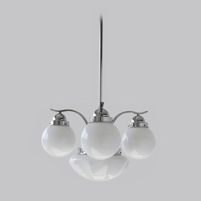 A Clérachic chrome 4-light glass globe chandelier hangs unlit, vented caps on the white globes against grey.