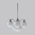 A Clérachic chrome 4-light glass globe chandelier hangs unlit, vented caps on the white globes against grey.