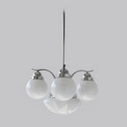A Clérachic chrome 4-light glass globe chandelier hangs unlit, vented caps on the white globes against grey.