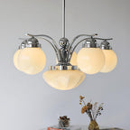 Clérachic 6-light chrome glass globe chandelier lit over a table with books, a jar, and a gold vase of dried stems.