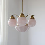 Clérachic 4-light glass globe chandelier in copper-plated metal hanging beside a sheer white curtain in a bright room.