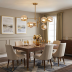Amber glass globes glow on this Clérachic gold chandelier above a dining table set with wine glasses and cream upholstered chairs.