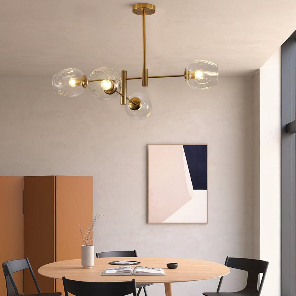 Clear glass globes on a gold Clérachic chandelier above a round wooden table and black folding chairs, with a pink-and-navy print.