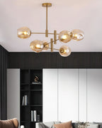 Amber globes on a gold-finish Clérachic chandelier below a white ceiling, with black slatted panelling and shelving behind.