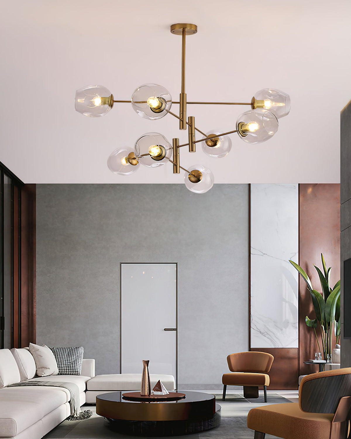 Clear glass globes lit on a gold branching Clérachic chandelier in a high-ceilinged room with a white sofa and tan armchairs.