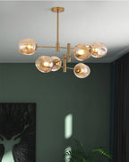 Amber globes on a gold Clérachic chandelier against a deep green wall, with a dark curtain and a stag print below.