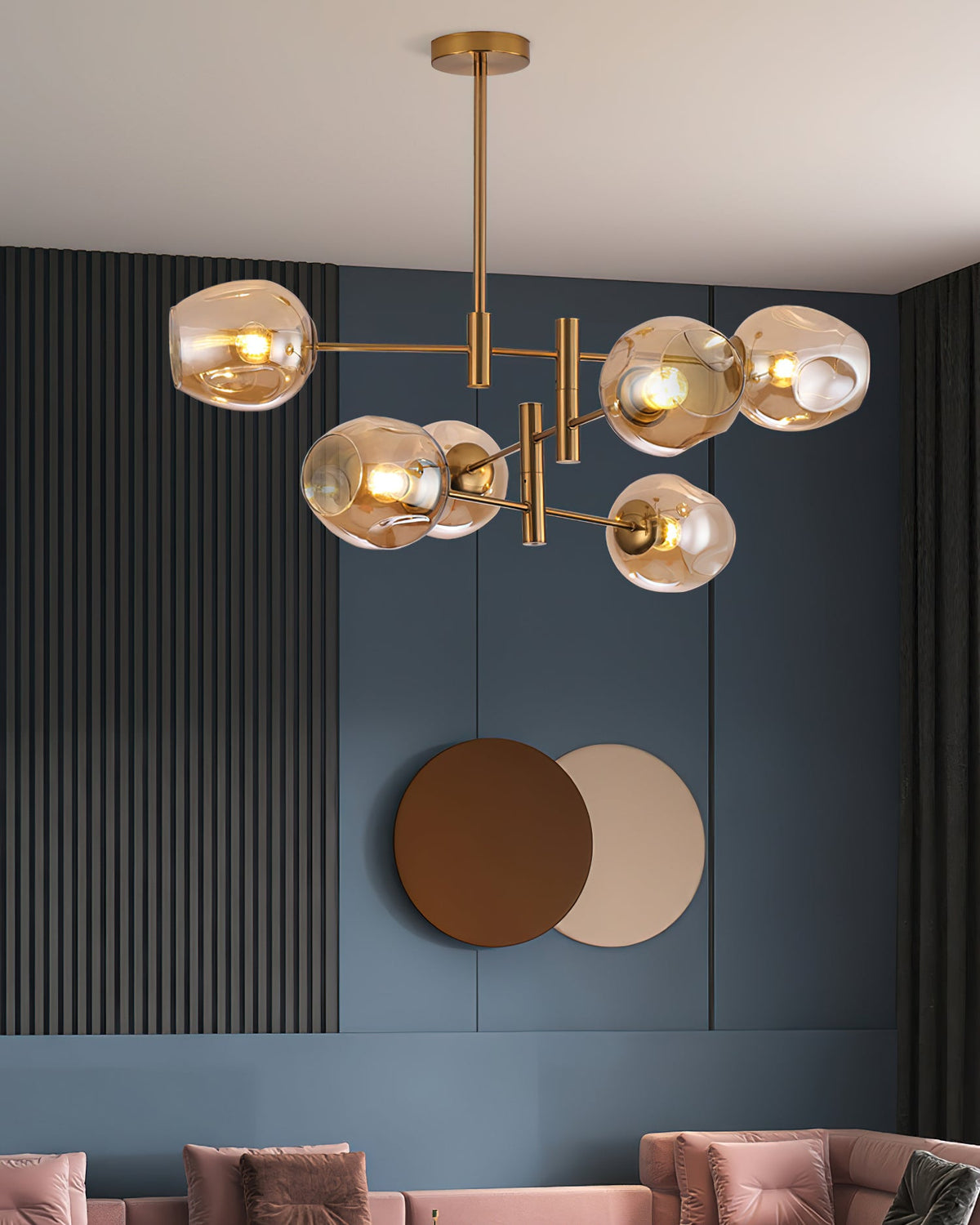 Lit amber globes on a Clérachic gold chandelier in front of a blue panelled wall with two round wall discs and pink seating.