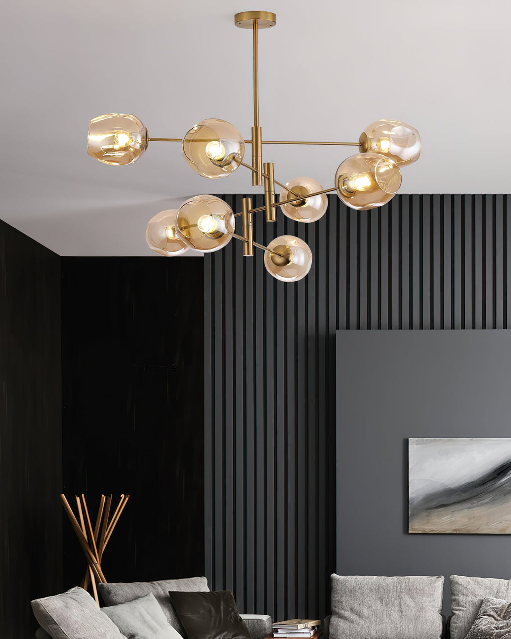 Amber glass globes glowing on a gold-finish Clérachic chandelier above a living room with dark slatted wall panels and a grey sofa.