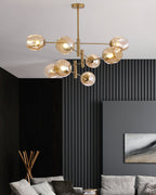 Amber glass globes glowing on a gold-finish Clérachic chandelier above a living room with dark slatted wall panels and a grey sofa.