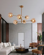 Amber globes lit on a branching Clérachic chandelier in an open living space with a white sofa, a round coffee table and tan chairs.