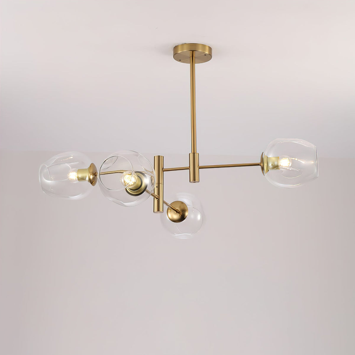 Four clear glass globes on a gold-finish chandelier seen from below against a pale ceiling, a Clérachic ceiling-mounted design.