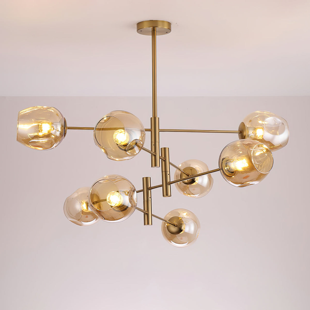 Lit amber globes on the branching gold arms of this Clérachic chandelier, photographed against a soft grey-lilac ceiling.