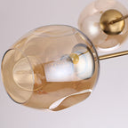 Close view of an amber glass globe with a dimpled rim and its brass cap and bulb on this Clérachic chandelier.