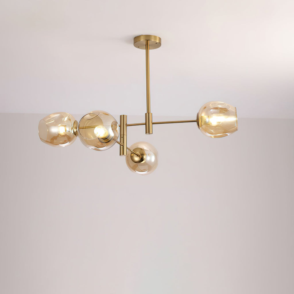 Four-globe Clérachic chandelier in amber glass with gold arms and a rod, lit and photographed against a pale wall.