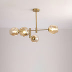 Four-globe Clérachic chandelier in amber glass with gold arms and a rod, lit and photographed against a pale wall.