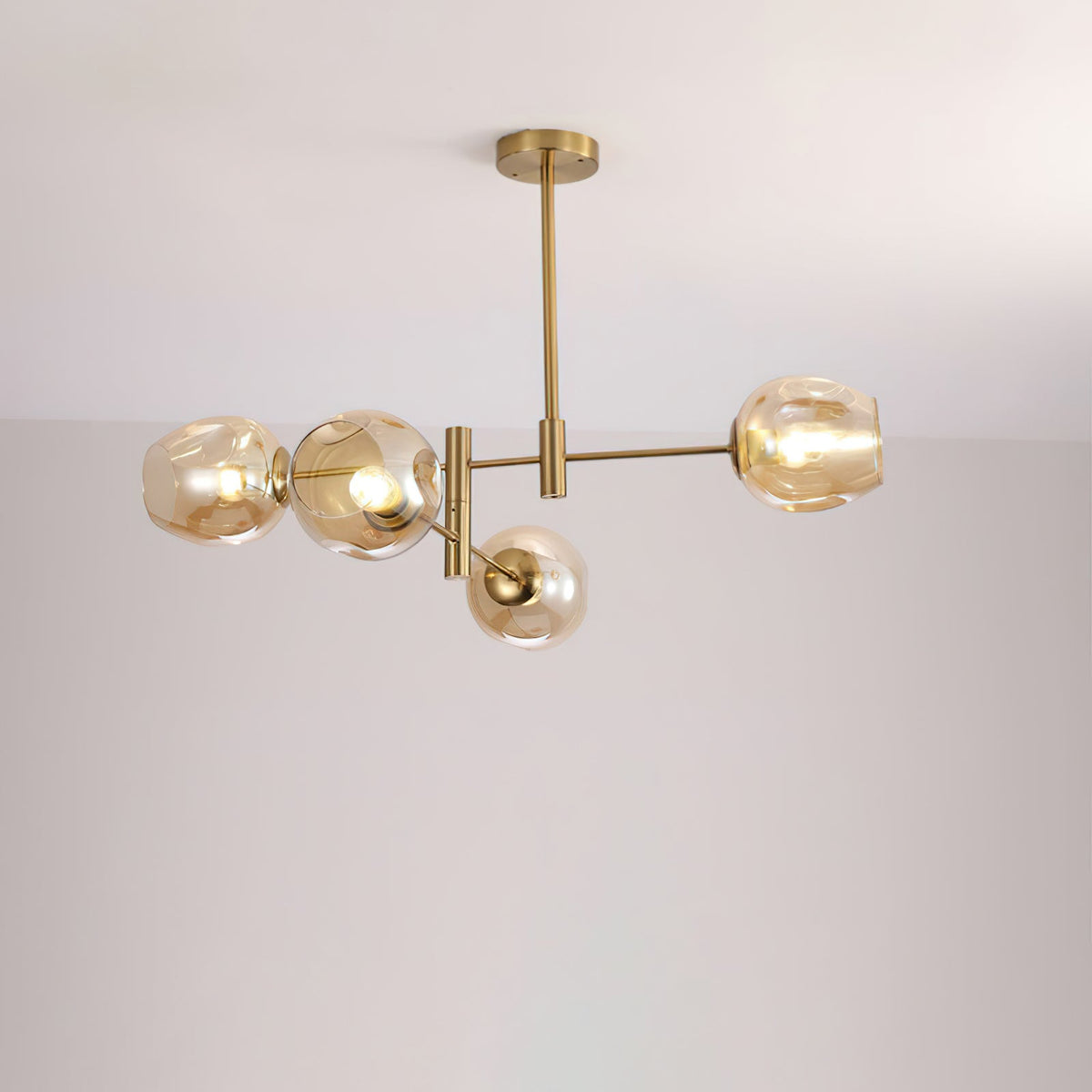 Four-globe Clérachic chandelier in amber glass with gold arms and a rod, lit and photographed against a pale wall.