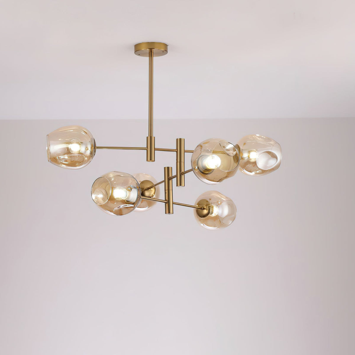 Amber-toned glass globes lit on a smaller gold-finish Clérachic chandelier hung from a slim rod, against a soft grey wall.