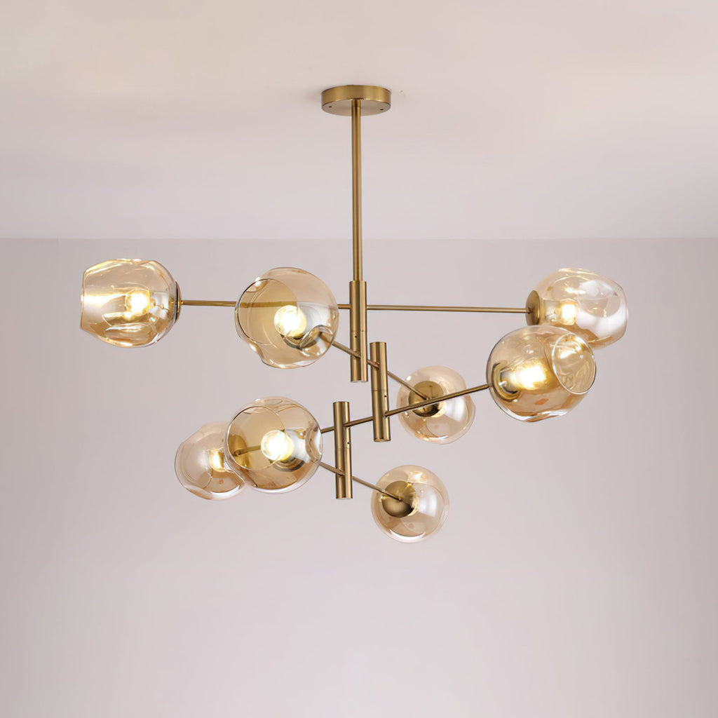 Amber globes lit on a larger gold-finish Clérachic chandelier with several tiers of arms, seen against a pale grey wall.