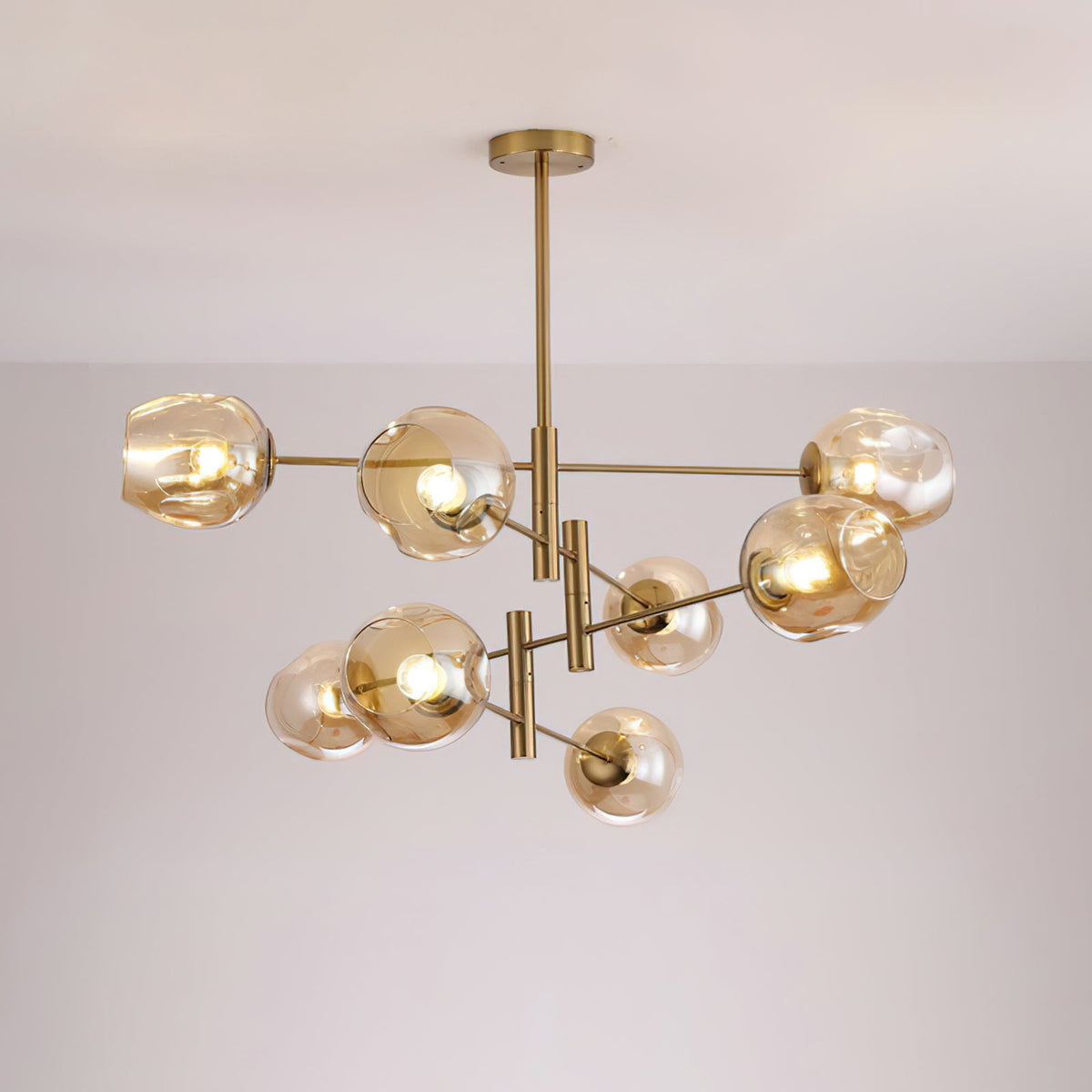 Amber globes lit on a larger gold-finish Clérachic chandelier with several tiers of arms, seen against a pale grey wall.