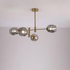 Four smoky grey glass globes lit on a gold-finish Clérachic chandelier with a slim rod, against a pale wall.