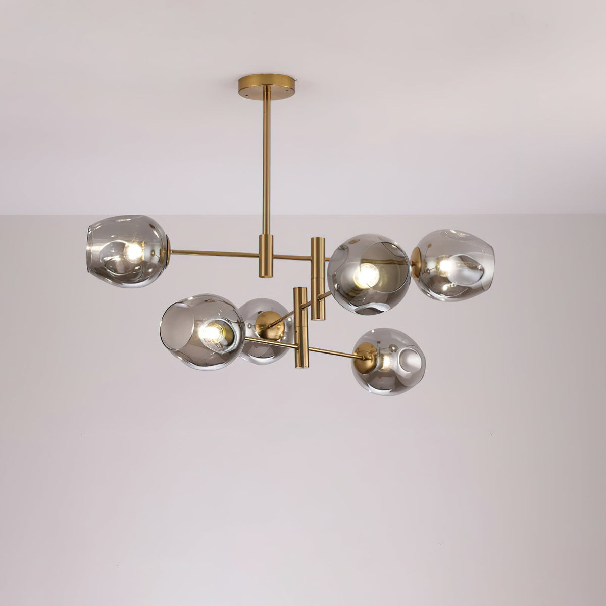 Smoky grey dimpled globes lit on the gold arms of this Clérachic chandelier, seen below a pale ceiling.