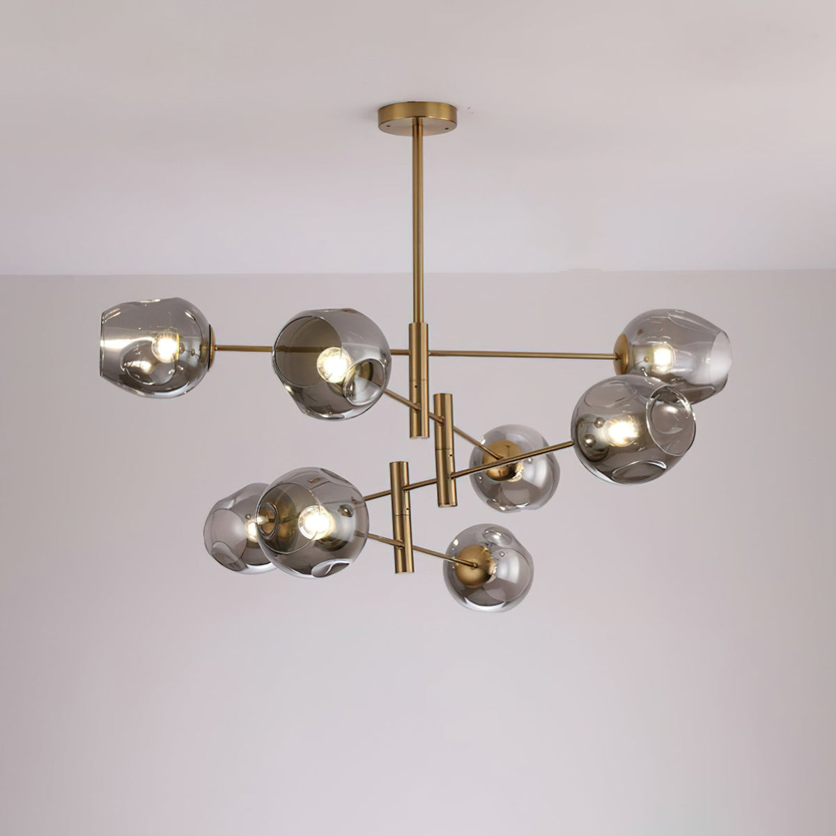 Larger Clérachic gold chandelier with smoky grey glass globes on several tiers of arms, lit against a pale wall.