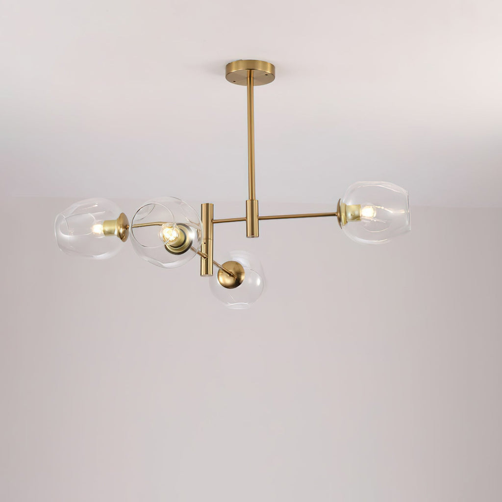 Four clear glass globes lit on a gold-finish Clérachic chandelier with a slim ceiling rod, against a pale wall.