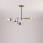 Four clear glass globes lit on a gold-finish Clérachic chandelier with a slim ceiling rod, against a pale wall.