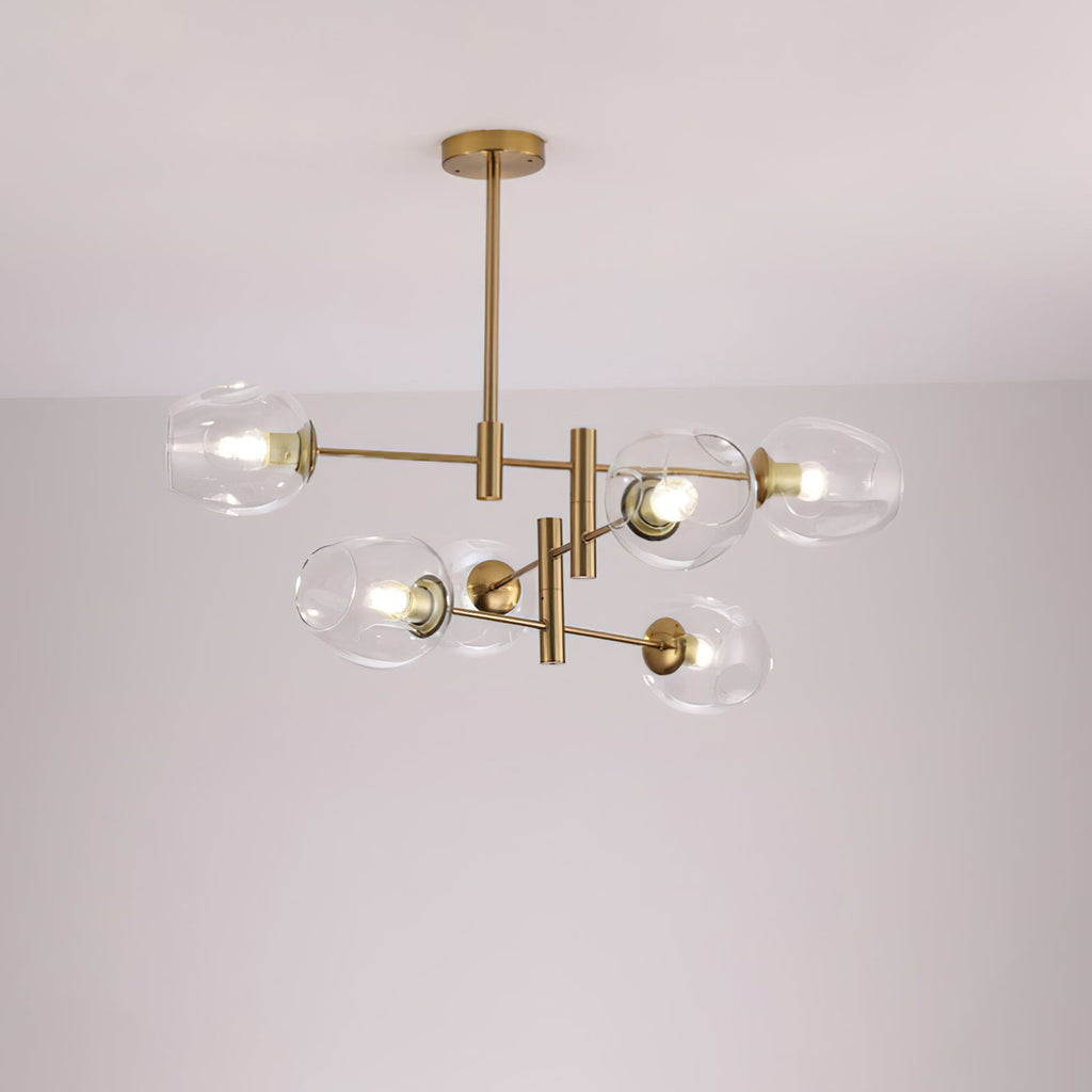 Clear glass globes with bulbs visible on a gold-finish Clérachic chandelier, lit and photographed against a pale ceiling.