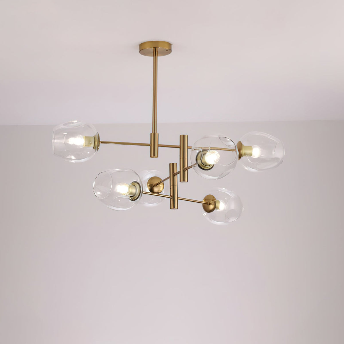 Clear glass globes with bulbs visible on a gold-finish Clérachic chandelier, lit and photographed against a pale ceiling.