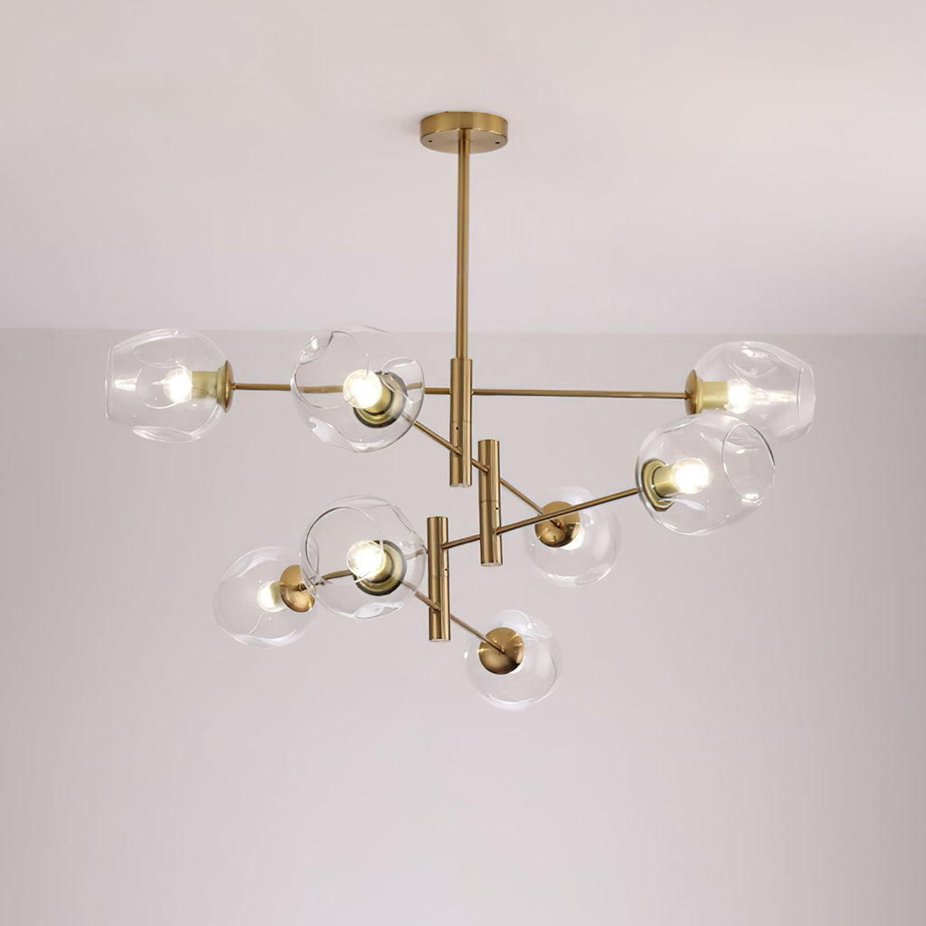 Clear dimpled glass globes on the layered gold arms of a larger Clérachic chandelier, lit against a pale wall.