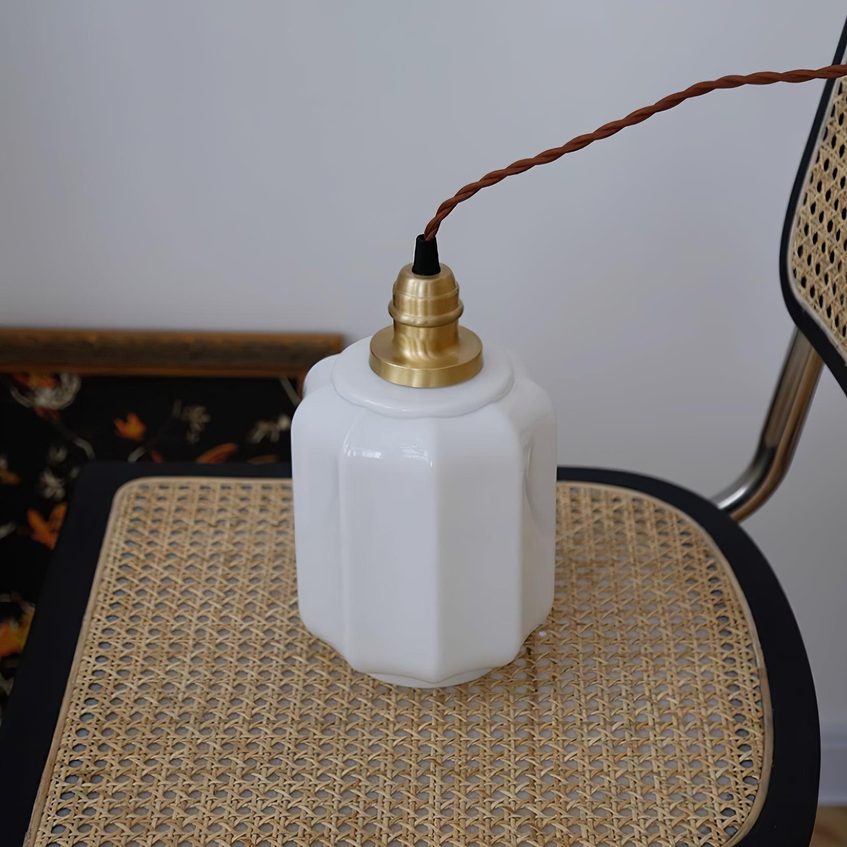 Close-up of the Clérachic glass globe pendant light's brass fitting, shade resting on a woven rattan chair.