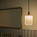 Clérachic glass globe pendant light illuminating a bathroom beside a brass-framed mirror and ribbed tile wall.