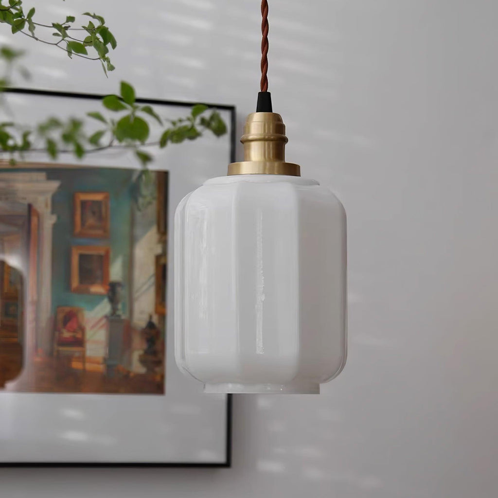 Clérachic glass globe pendant light hanging at an angle near framed wall art and trailing green leaves overhead.