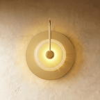 Clérachic single-head wall lamp with a brass disc backplate, a curved brass arm and a lit clear textured glass dome.