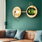 Clérachic two-head brass wall lamp, clear and green glass domes, joined by a horizontal arm on a teal wall above a tan leather sofa.