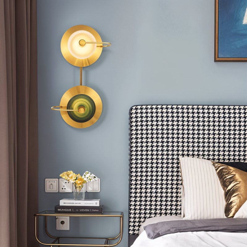 Clérachic two-head brass wall lamp with clear and green glass domes beside a houndstooth headboard on a soft blue wall.
