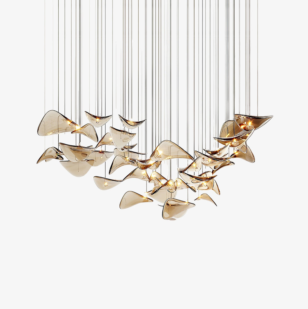 Dozens of amber glass leaves hang on fine cables in a sweeping curve, this Clérachic leaf pendant light shown on a white backdrop.