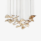 Dozens of amber glass leaves hang on fine cables in a sweeping curve, this Clérachic leaf pendant light shown on a white backdrop.