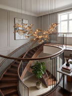 A Clérachic leaf pendant light hangs beside a landing with a dark curved stair rail, a large window and a potted fig below.