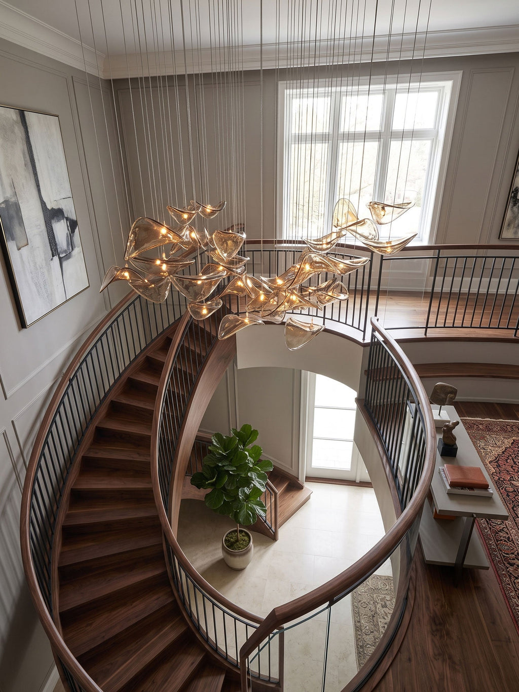 Glowing amber leaves of this Clérachic pendant hang near a grey-panelled wall and a window, above a curved staircase.