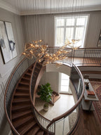 Glowing amber leaves of this Clérachic pendant hang near a grey-panelled wall and a window, above a curved staircase.