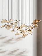 Amber glass leaf pendant from Clérachic, lit, with soft leaf-shaped shadows falling across the pale wall behind it.