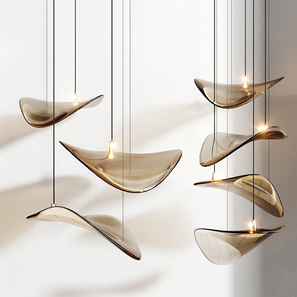 Six amber glass leaves hung close together on separate cables, each lifted at one edge, from this Clérachic pendant light.