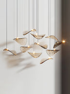Eleven amber glass leaves on thin cables, seen from a low angle, with small lights at their centres in this Clérachic pendant.