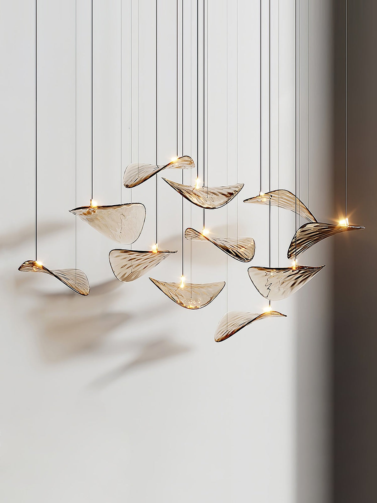 Eleven amber glass leaves on thin cables, seen from a low angle, with small lights at their centres in this Clérachic pendant.