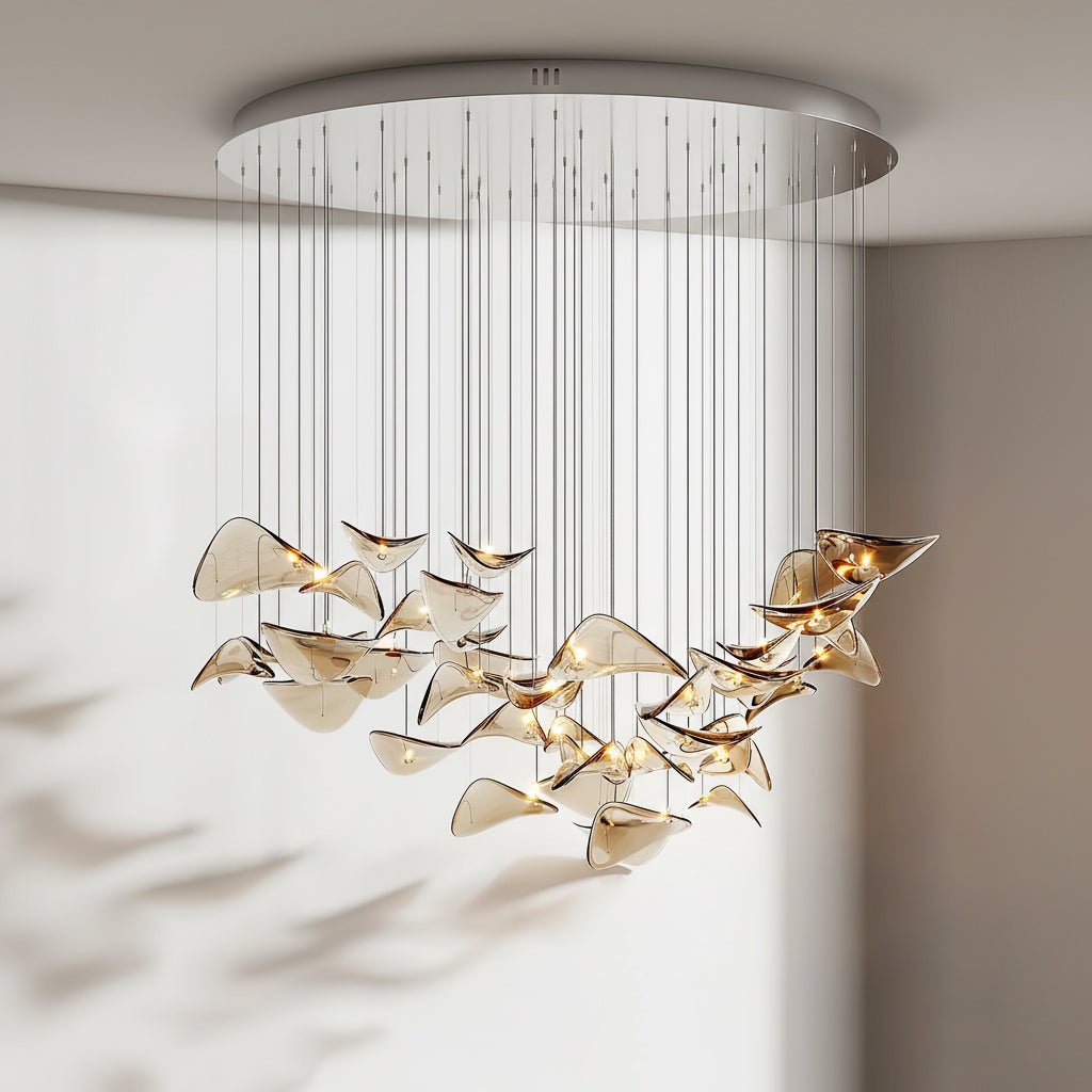 Round chrome ceiling plate with a wide group of amber glass leaves hanging below it on slim cables, from Clérachic.