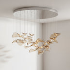 Round brushed-metal canopy with amber glass leaves on cables, hung in a pale room, from this Clérachic pendant light.